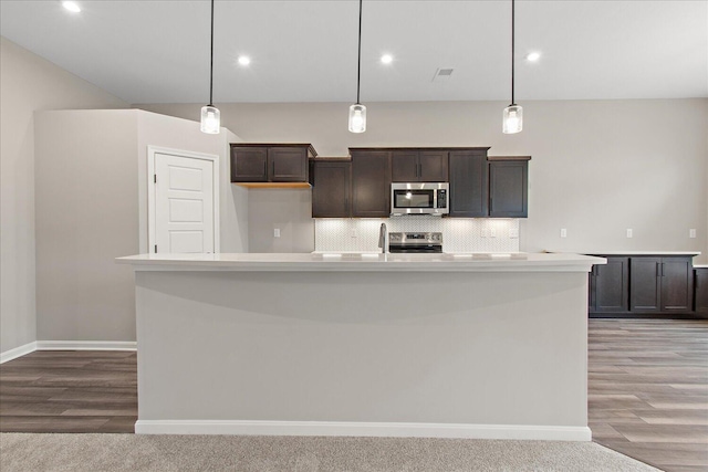 kitchen featuring stainless steel appliances, light countertops, a kitchen island with sink, and pendant lighting