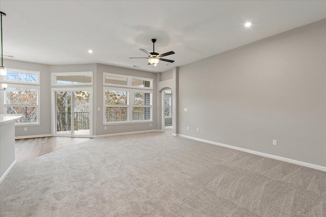 unfurnished living room featuring carpet floors, arched walkways, plenty of natural light, and baseboards