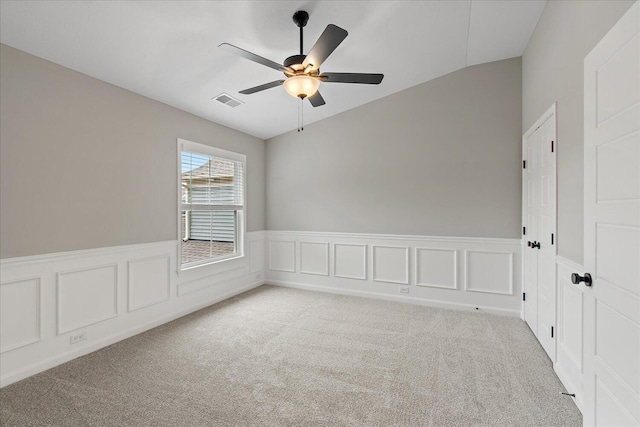 empty room with wainscoting, visible vents, a ceiling fan, and light colored carpet