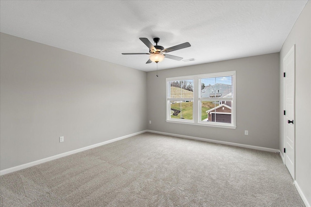 spare room with light colored carpet, ceiling fan, a textured ceiling, and baseboards