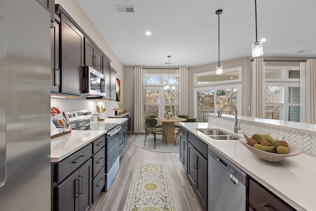 kitchen with stainless steel appliances, a sink, hanging light fixtures, light countertops, and dark brown cabinets