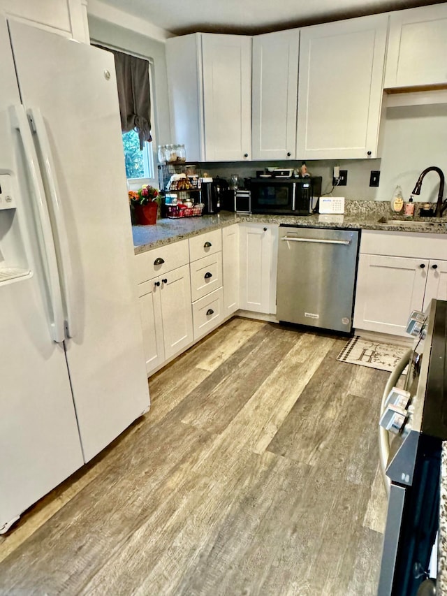 kitchen featuring light wood-type flooring, sink, white refrigerator with ice dispenser, dishwasher, and white cabinetry