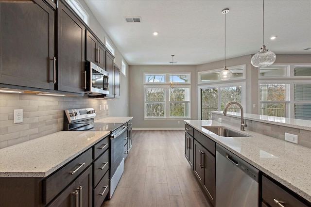 kitchen with sink, tasteful backsplash, light stone counters, hanging light fixtures, and appliances with stainless steel finishes