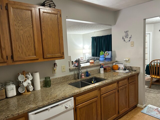 kitchen with white dishwasher, a textured ceiling, sink, light stone countertops, and light wood-type flooring