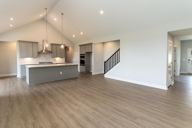 kitchen with gray cabinetry, a center island with sink, extractor fan, decorative light fixtures, and dark hardwood / wood-style floors