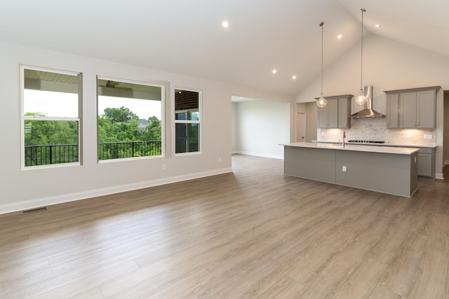 kitchen featuring range hood, light wood-type flooring, decorative light fixtures, gray cabinets, and a kitchen island with sink