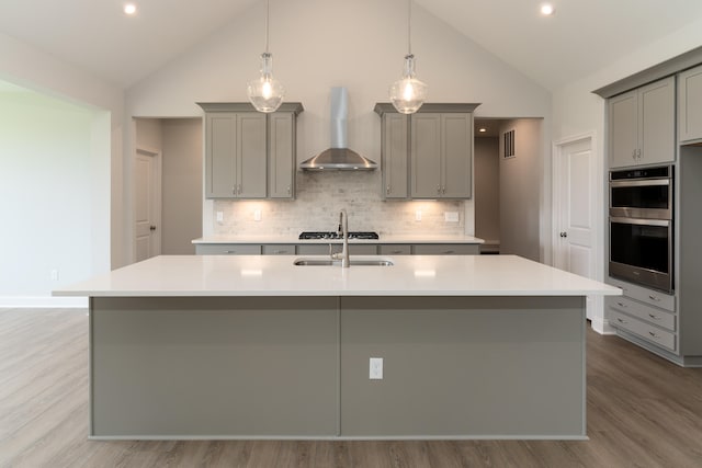 kitchen featuring wall chimney exhaust hood, a center island with sink, and gray cabinetry