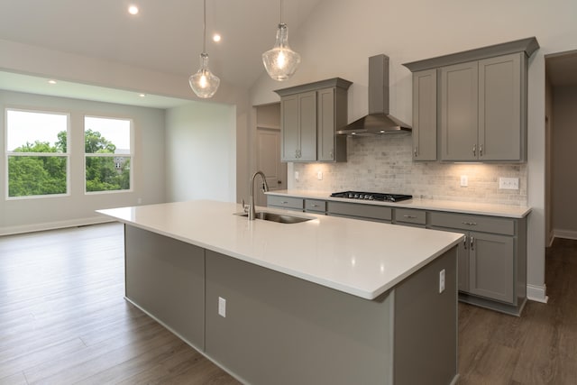 kitchen featuring an island with sink, gray cabinets, wall chimney range hood, and vaulted ceiling