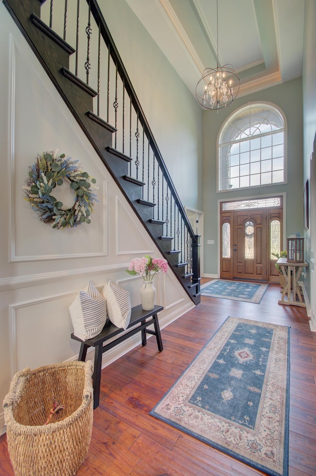 foyer entrance with crown molding, an inviting chandelier, a high ceiling, a tray ceiling, and dark hardwood / wood-style flooring