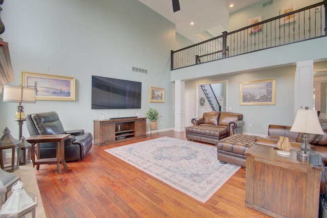 living room featuring ceiling fan, wood-type flooring, a high ceiling, and ornate columns