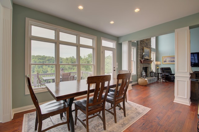 dining area featuring a stone fireplace, dark hardwood / wood-style floors, and ornate columns