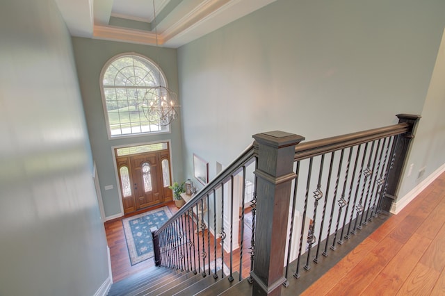 entrance foyer featuring crown molding, an inviting chandelier, wood-type flooring, a raised ceiling, and a towering ceiling