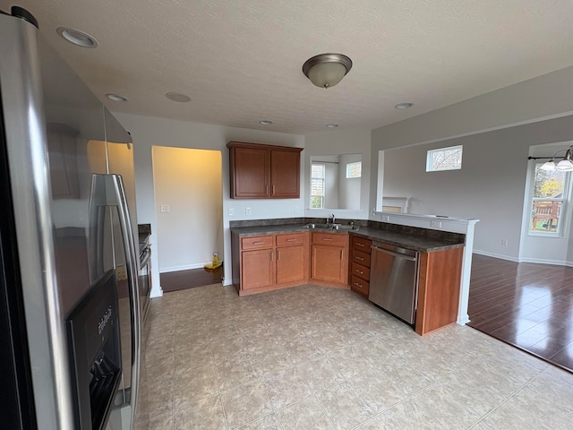 kitchen featuring light hardwood / wood-style floors, sink, kitchen peninsula, appliances with stainless steel finishes, and a textured ceiling