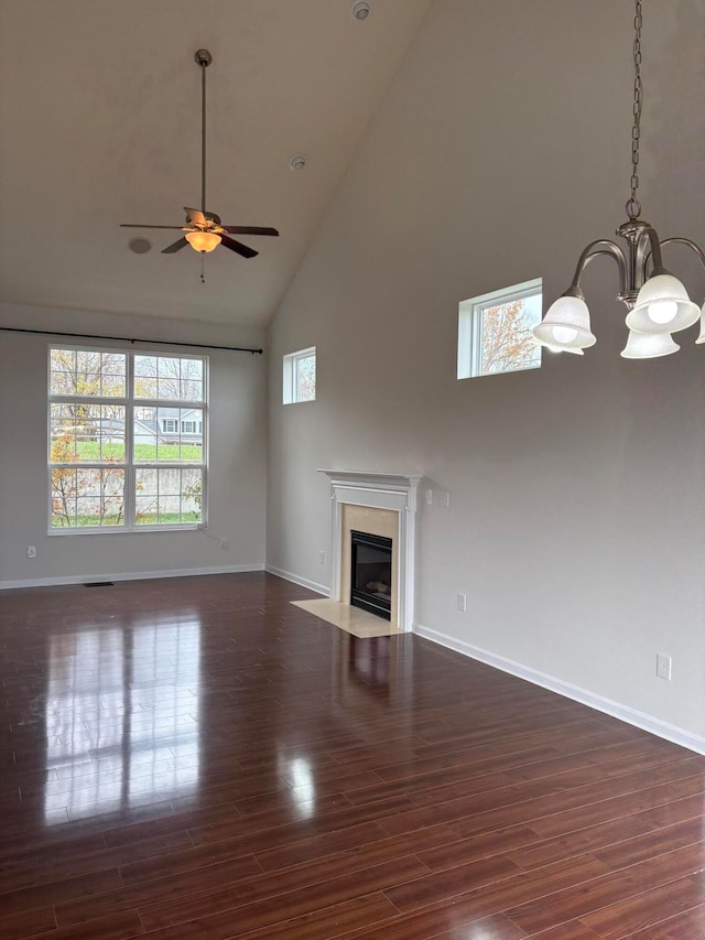 unfurnished living room with high vaulted ceiling, ceiling fan with notable chandelier, and dark wood-type flooring