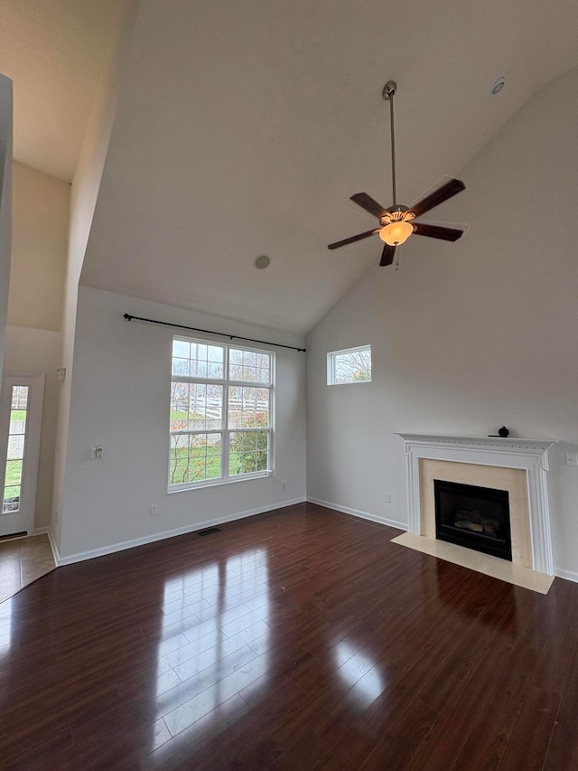 unfurnished living room with ceiling fan, high vaulted ceiling, a healthy amount of sunlight, and dark hardwood / wood-style flooring