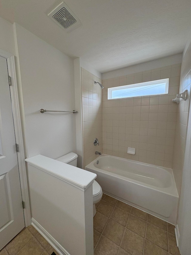 bathroom featuring tile patterned floors, toilet, a textured ceiling, and tiled shower / bath combo