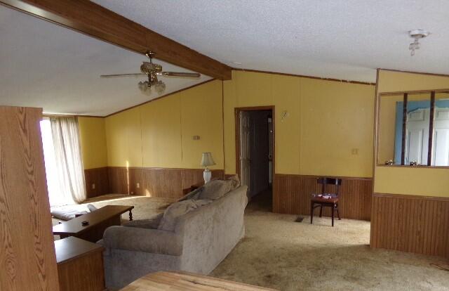 living room with light colored carpet, wood walls, a textured ceiling, ceiling fan, and lofted ceiling with beams