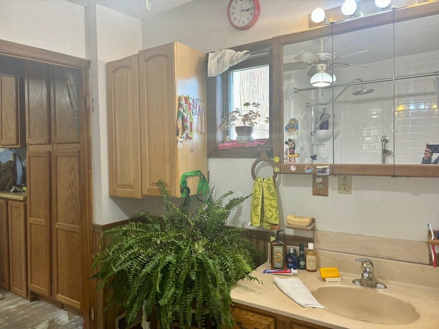 bathroom featuring ceiling fan, vanity, a textured ceiling, and tiled shower