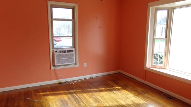 empty room featuring plenty of natural light, cooling unit, and wood-type flooring