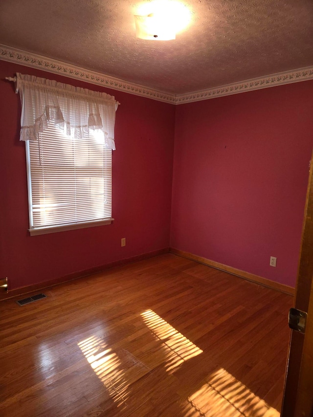 empty room featuring wood-type flooring, a textured ceiling, and ornamental molding