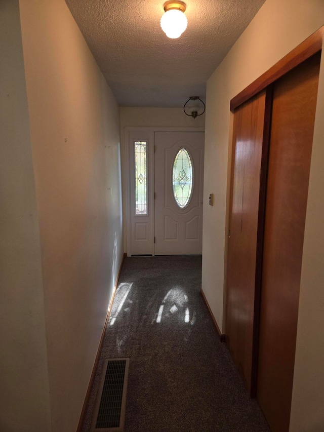 doorway to outside featuring a textured ceiling and dark colored carpet