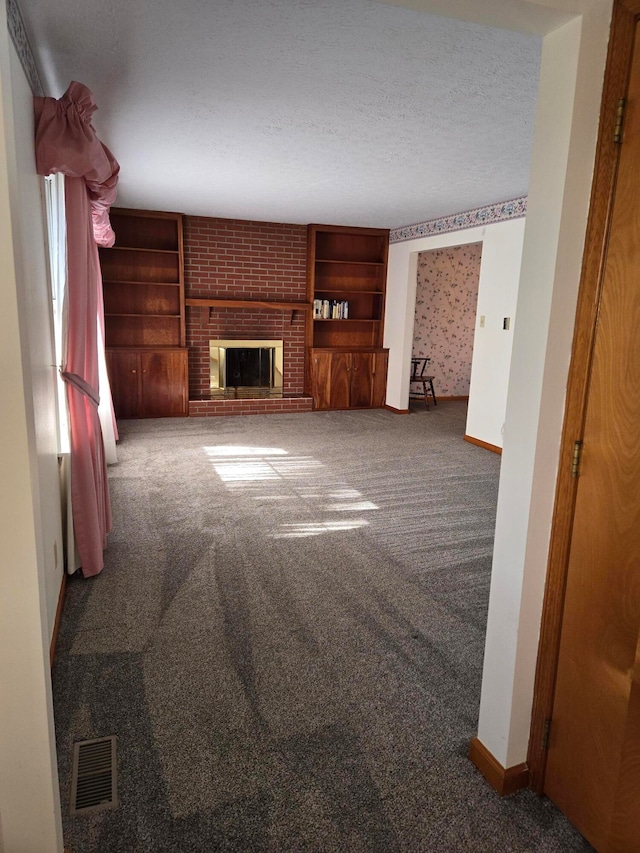 unfurnished living room featuring carpet, a textured ceiling, and a brick fireplace