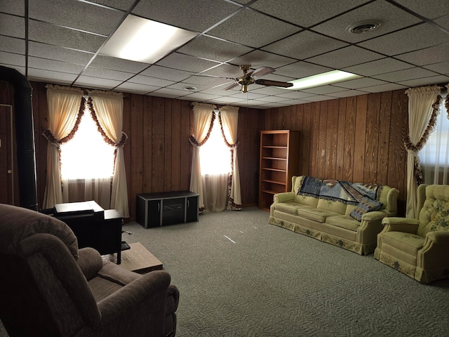 carpeted living room with wood walls, a drop ceiling, and ceiling fan