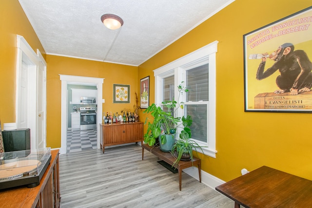 hallway featuring a textured ceiling, light wood-type flooring, and ornamental molding