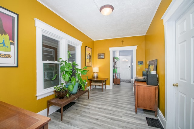 corridor featuring a textured ceiling, light hardwood / wood-style floors, and ornamental molding