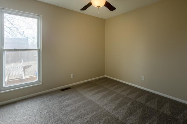 spare room with plenty of natural light, visible vents, dark carpet, and baseboards