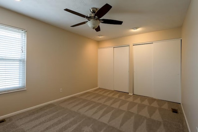 unfurnished bedroom with ceiling fan, light carpet, visible vents, baseboards, and multiple closets