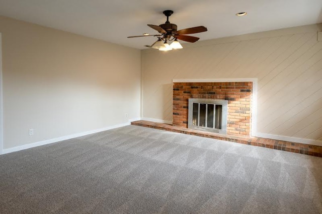 unfurnished living room with baseboards, ceiling fan, carpet floors, wood walls, and a fireplace