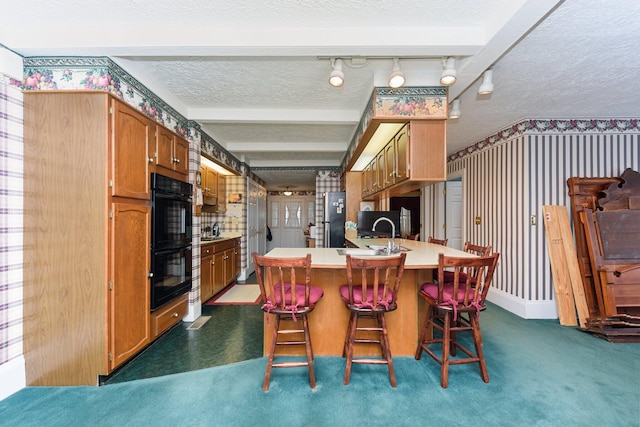 kitchen with track lighting, a kitchen breakfast bar, stainless steel fridge, a textured ceiling, and double oven