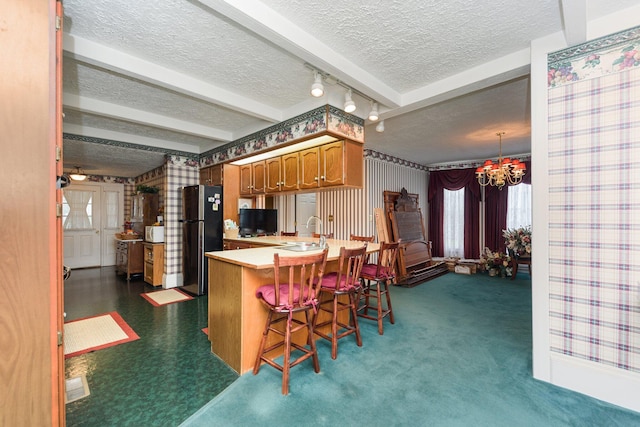 kitchen with a kitchen bar, kitchen peninsula, a notable chandelier, beamed ceiling, and stainless steel refrigerator