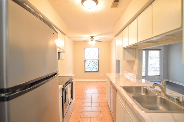 kitchen with appliances with stainless steel finishes, a textured ceiling, sink, light tile patterned floors, and white cabinetry