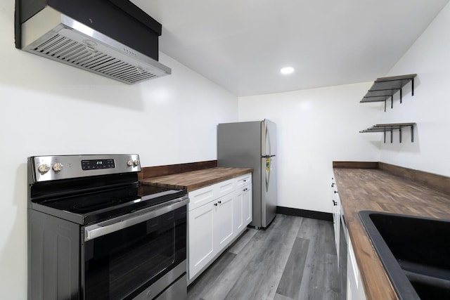 kitchen featuring butcher block counters, white cabinets, wall chimney range hood, appliances with stainless steel finishes, and wood-type flooring