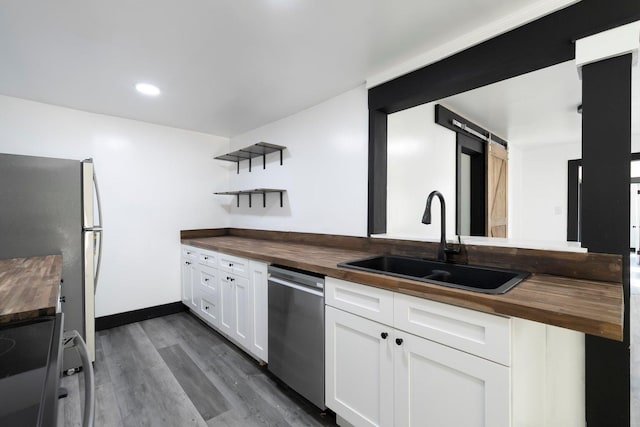 kitchen with wood counters, white cabinets, sink, a barn door, and appliances with stainless steel finishes