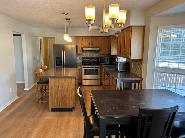 kitchen with appliances with stainless steel finishes, a center island, tasteful backsplash, hanging light fixtures, and light wood-type flooring