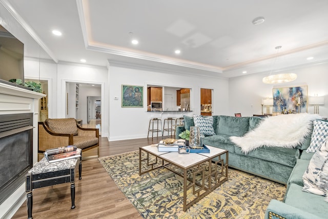 living room featuring hardwood / wood-style flooring, ornamental molding, a tray ceiling, and a chandelier