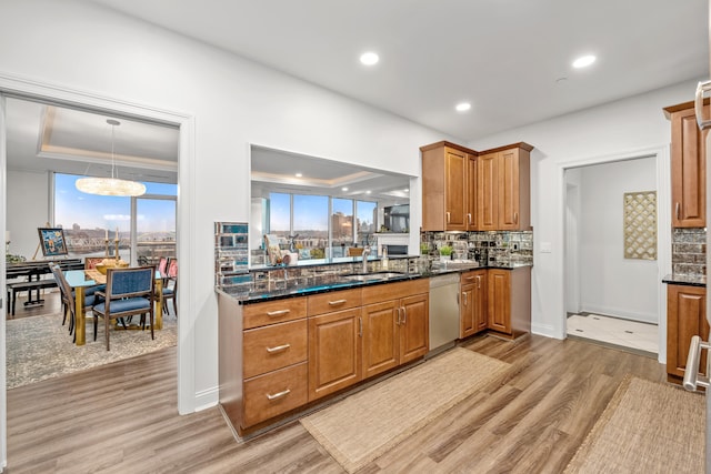 kitchen with a raised ceiling, sink, stainless steel dishwasher, tasteful backsplash, and light hardwood / wood-style floors