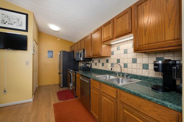 kitchen with backsplash, stainless steel appliances, vaulted ceiling, sink, and light hardwood / wood-style floors