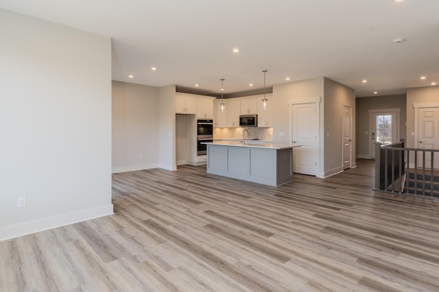 kitchen with tasteful backsplash, white cabinetry, stainless steel appliances, a center island with sink, and light wood-type flooring