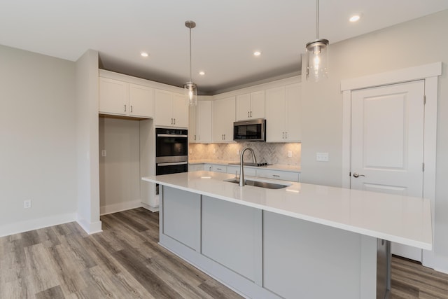 kitchen featuring an island with sink, hanging light fixtures, and white cabinets