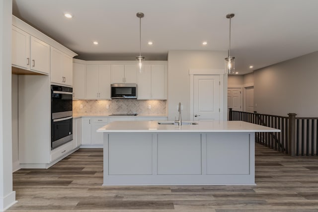 kitchen featuring sink, hanging light fixtures, an island with sink, stainless steel appliances, and white cabinets