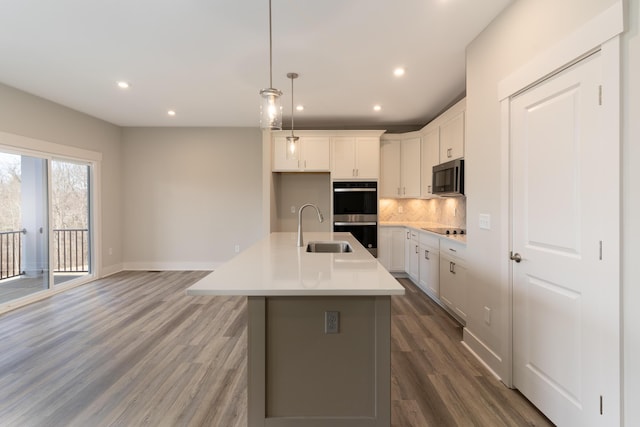 kitchen with double oven, white cabinetry, sink, a center island with sink, and black electric cooktop