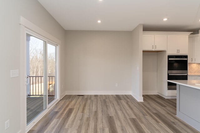 kitchen featuring double wall oven, white cabinets, light wood-type flooring, and decorative backsplash