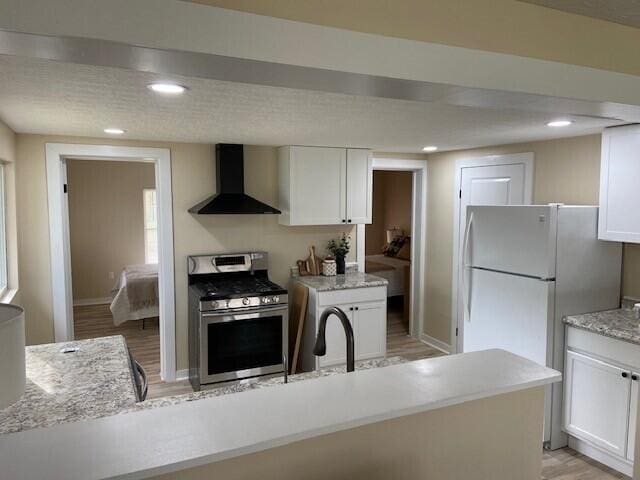 kitchen with gas range, light wood-type flooring, white cabinetry, and wall chimney exhaust hood