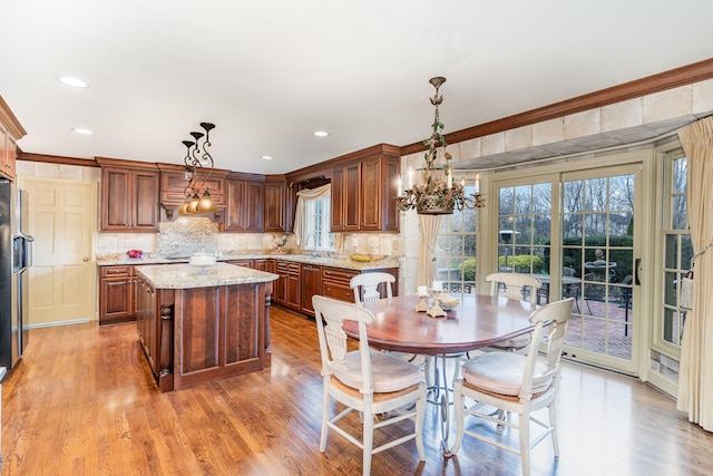 kitchen featuring light wood-type flooring, decorative light fixtures, a kitchen island, sink, and light stone counters