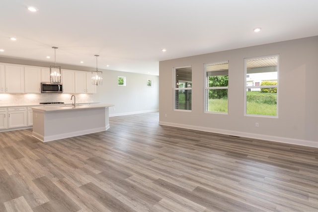 kitchen featuring stainless steel microwave, open floor plan, recessed lighting, a sink, and light wood-style flooring