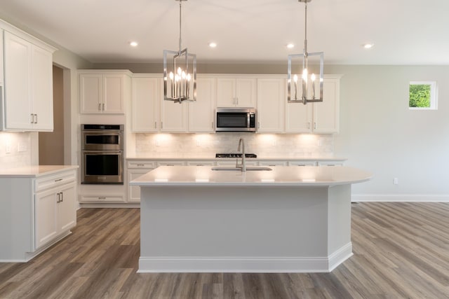 kitchen with stainless steel appliances, a chandelier, light countertops, light wood-style flooring, and a kitchen island with sink